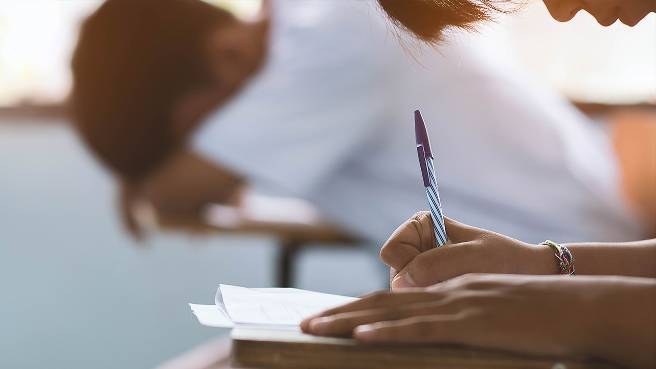 Photo of student taking exam and another stressed student laying his head on a desk