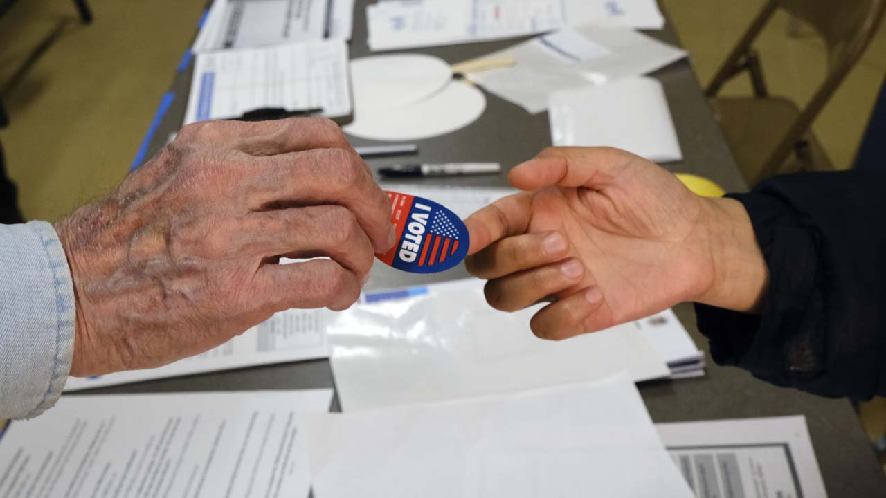 Photo of someone being handed an "I Voted" sticker