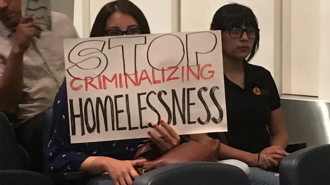 Photo of an audience member holding a sign that reads "Stop Criminalizing Homelessness"