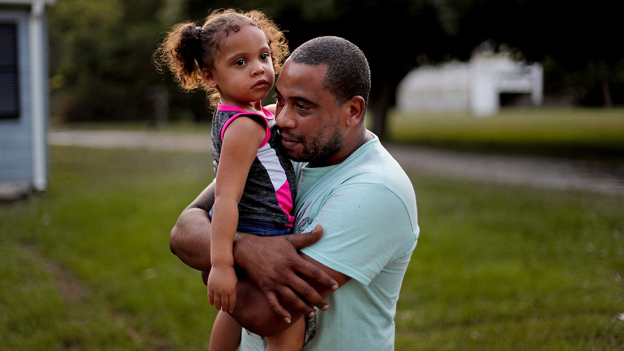 Photo of Jose Perez-Santiago, right, holding his daughter Jordalis, 2, as they return to their home for the first time since it was flooded