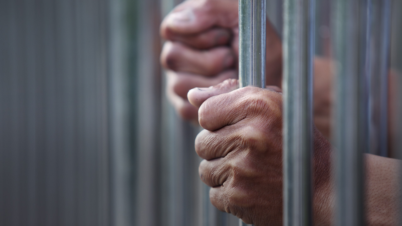 Prisoner hands gripping jail cell bars