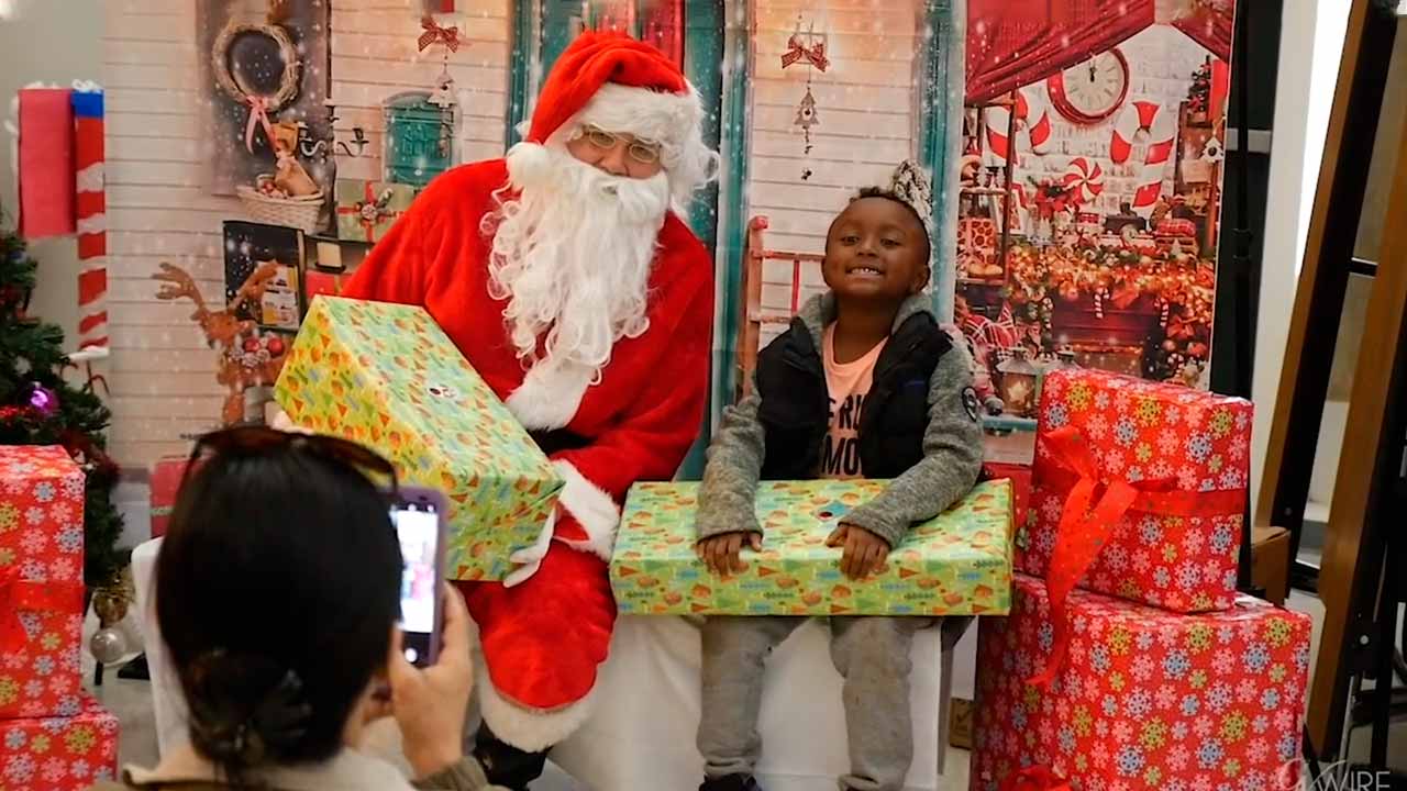 Photo of a young student sitting next to Santa Claus with a wrapped gift