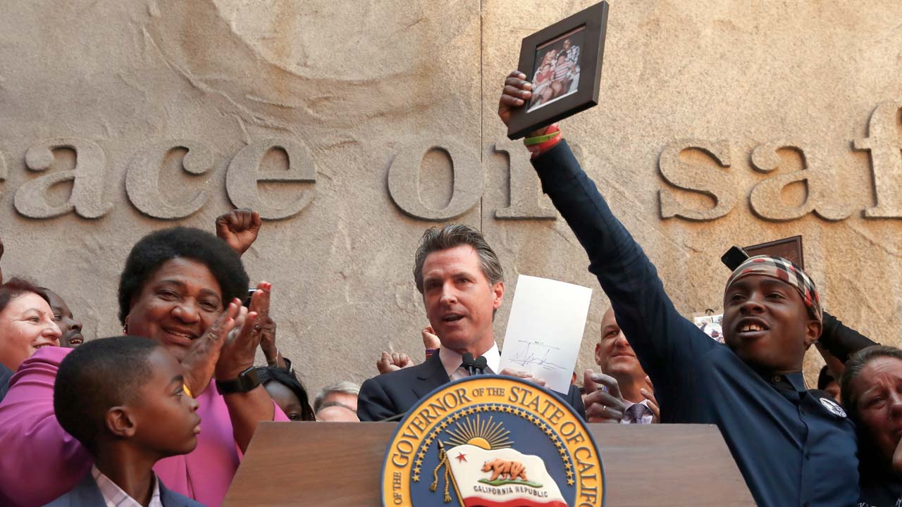 Photo of Gov. Gavin Newsom surrounded by Assemblywoman Shirley Weber and members of the Clark family after the signing of AB 392 lFam