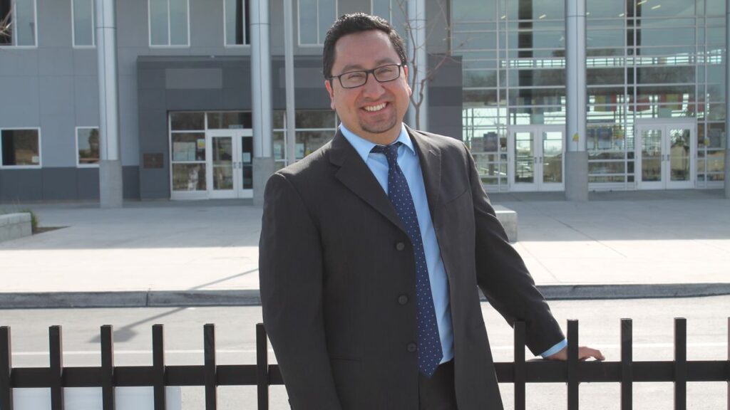 Environmental portrait of Rob Fuentes standing with his hand on the rail of a wrought-iron fence