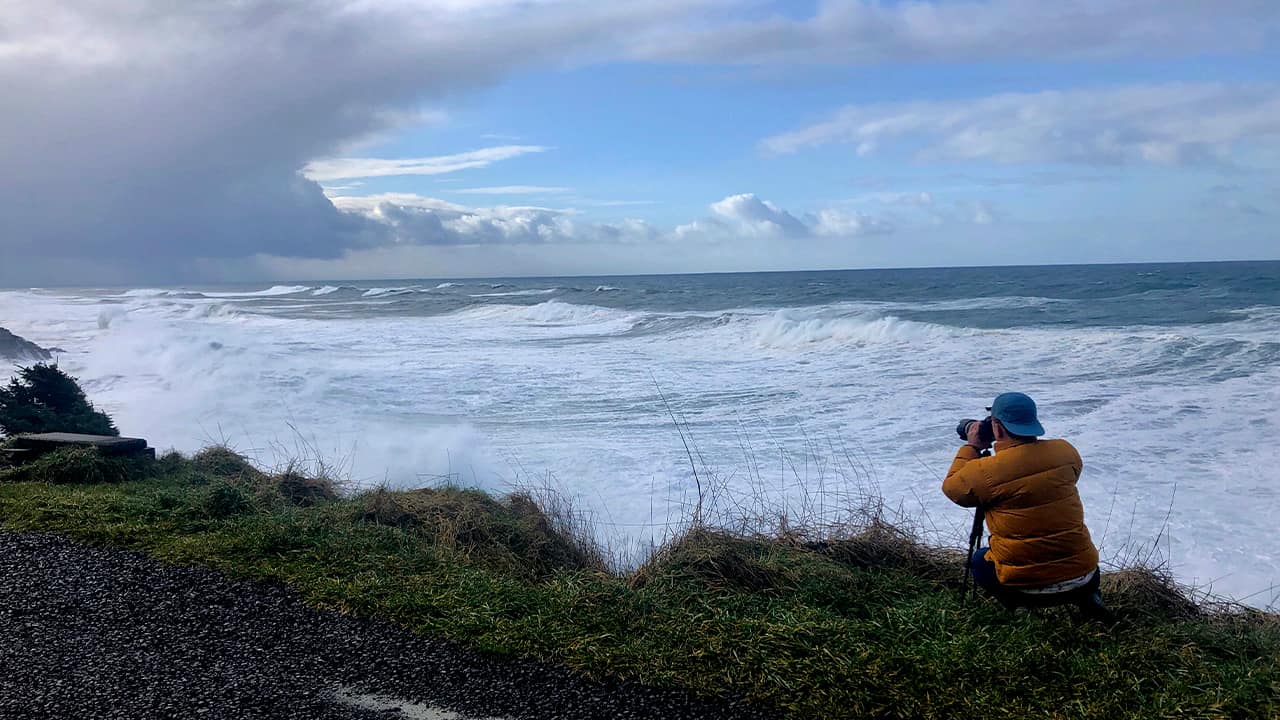Photo of a man photographing waves crashing onto the cliffs at Rodea Point in Lincoln County, Ore.