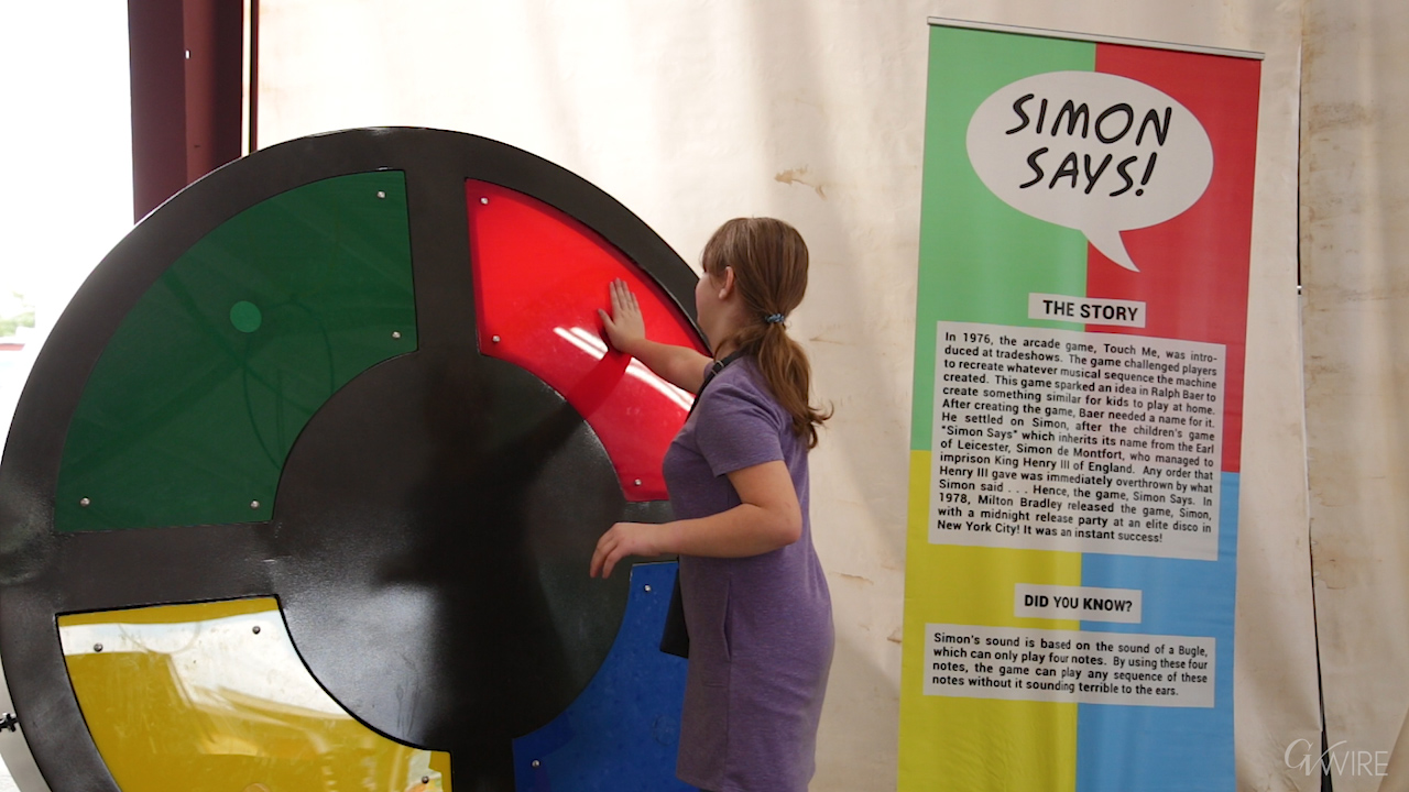 Young fair-goer plays with a large scale version of the electronic game Simon. 