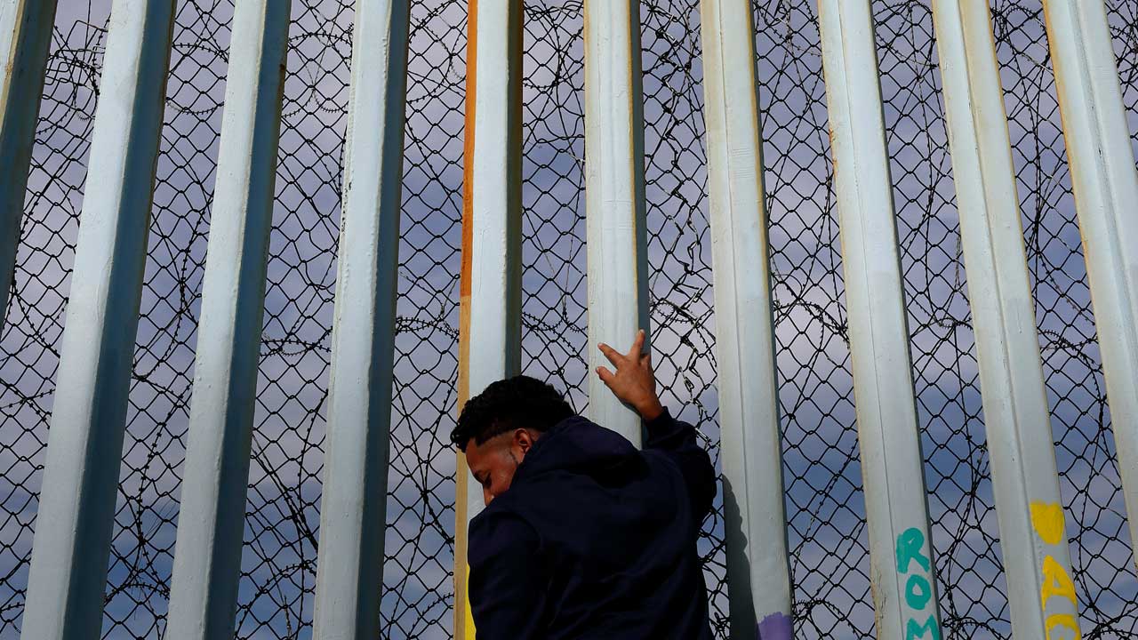 Photo of a man holding onto the border fence between the U.S. and Mexico