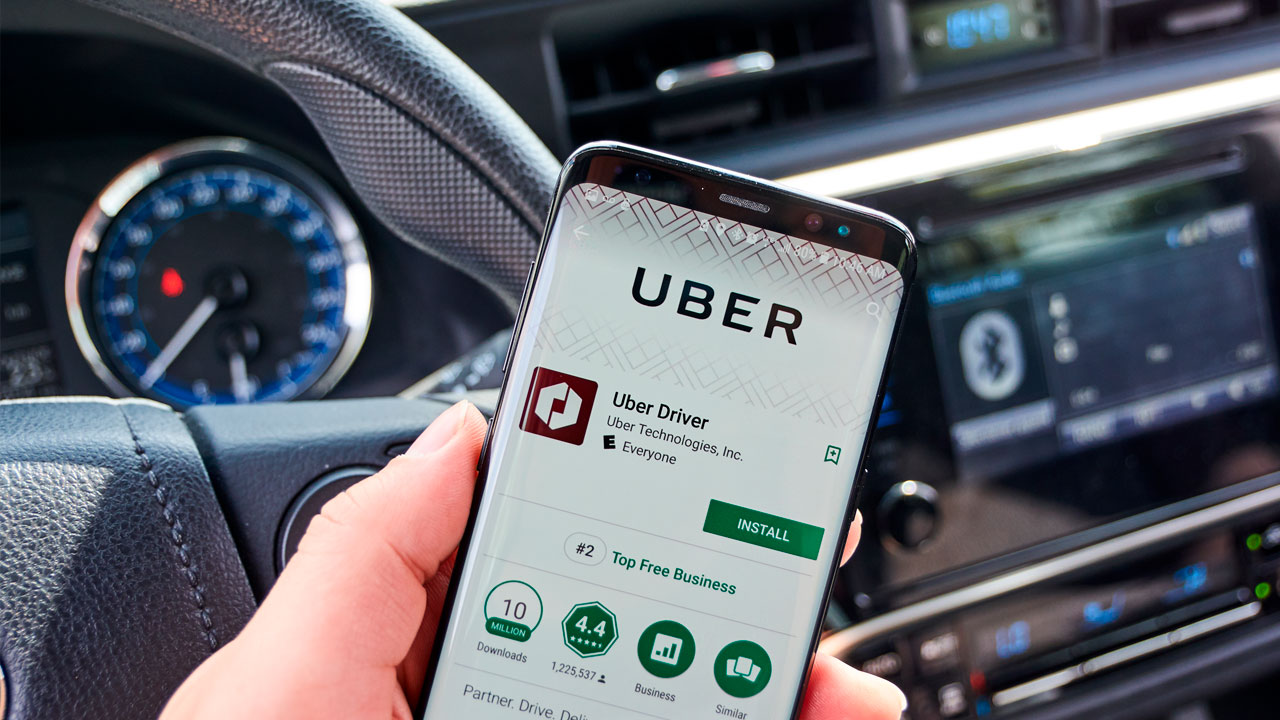 Uber driver inside car with ridesharing app displayed on smartphone.