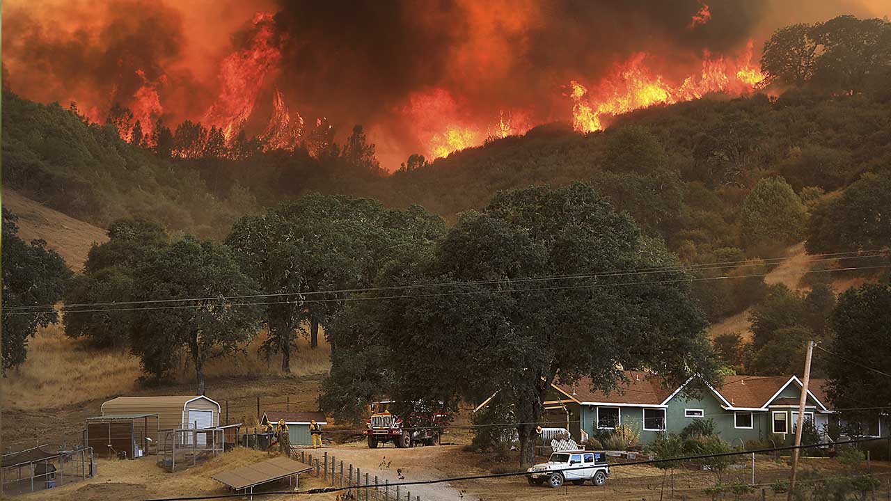 Wildfire burns on hills above rural home.