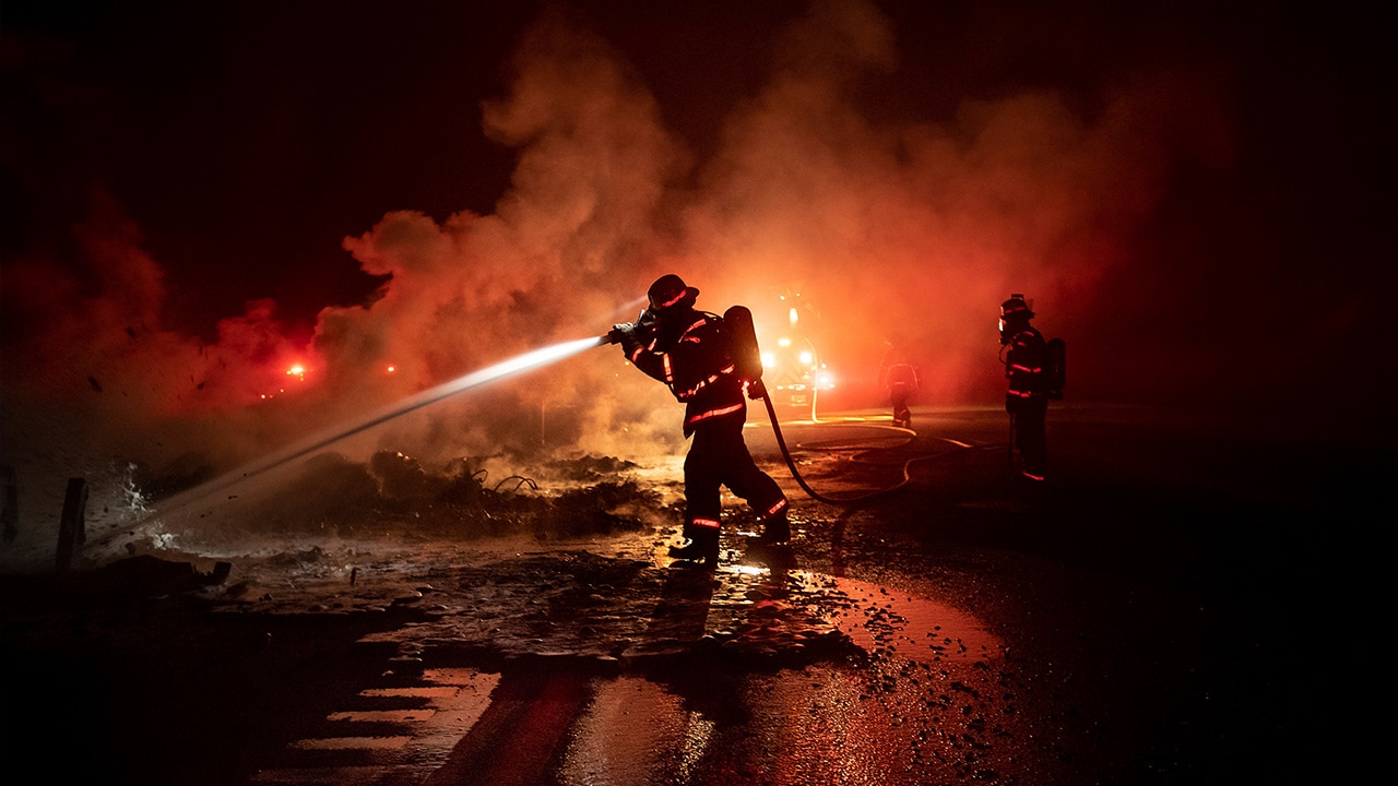 Photo of a firefighter spraying the remains of a vehicle