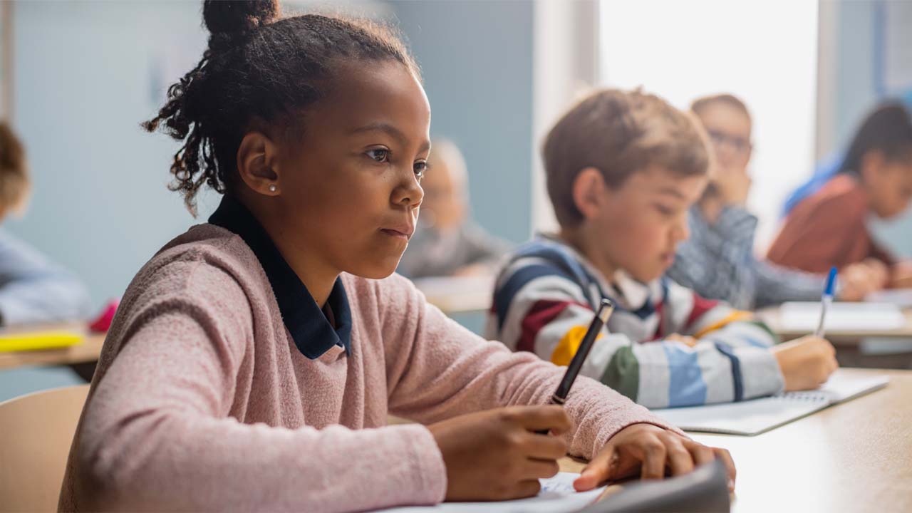 Image of children seated as their desks and working on their studies in a classroom