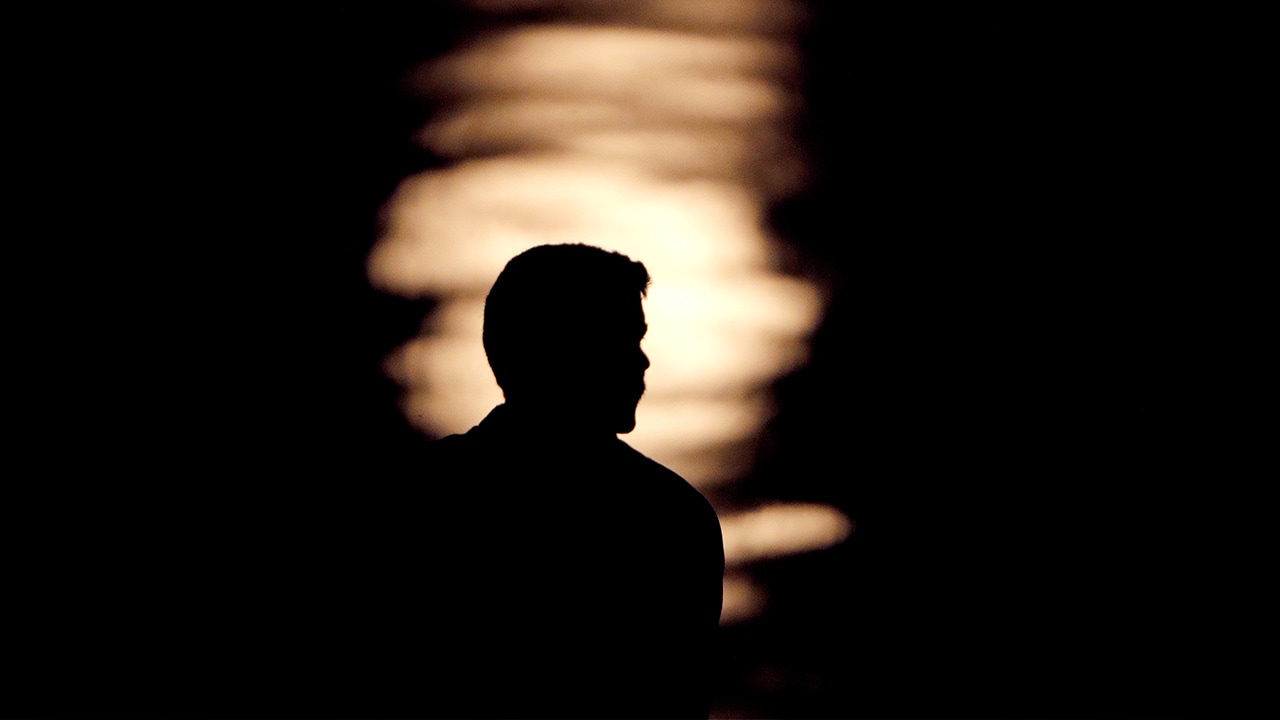 Photo of a man is silhouetted against moonlight reflecting off the Missouri River