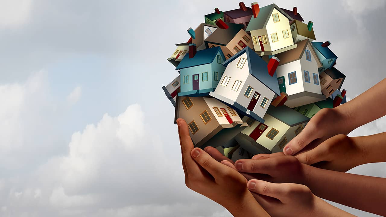 Composite of hands lifting up several toy houses. Image meant to convey affordable housing