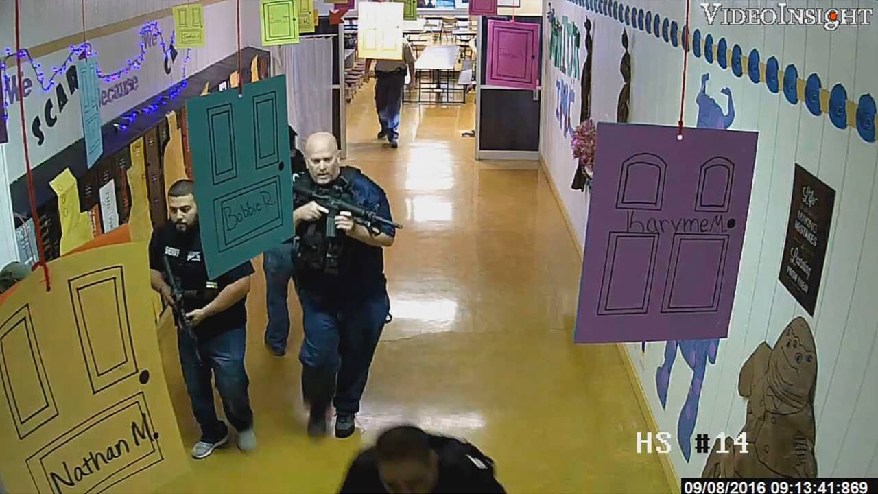 Photo of armed law enforcement officers move through a hallway at Alpine High School in Alpine, Texas