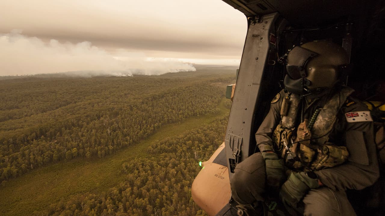 Photo of a Royal Australian Navy MRH-90 helicopter crew member looks out over fires burning near Cann River, Australia