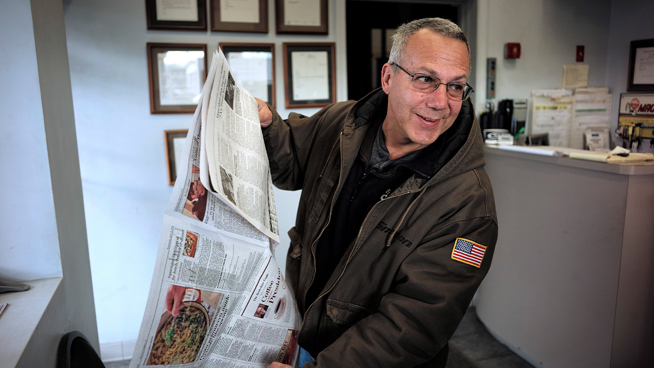 Photo of Phil Viscuso flipping through a copy of The Berkshire Eagle Newspaper 