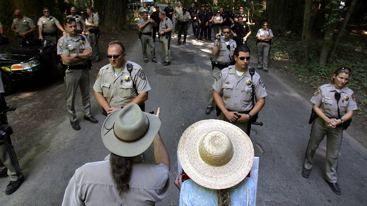 Photo of protestors trying to talk with CHP officers as they block off the entrance to the Bohemian Grove retreat