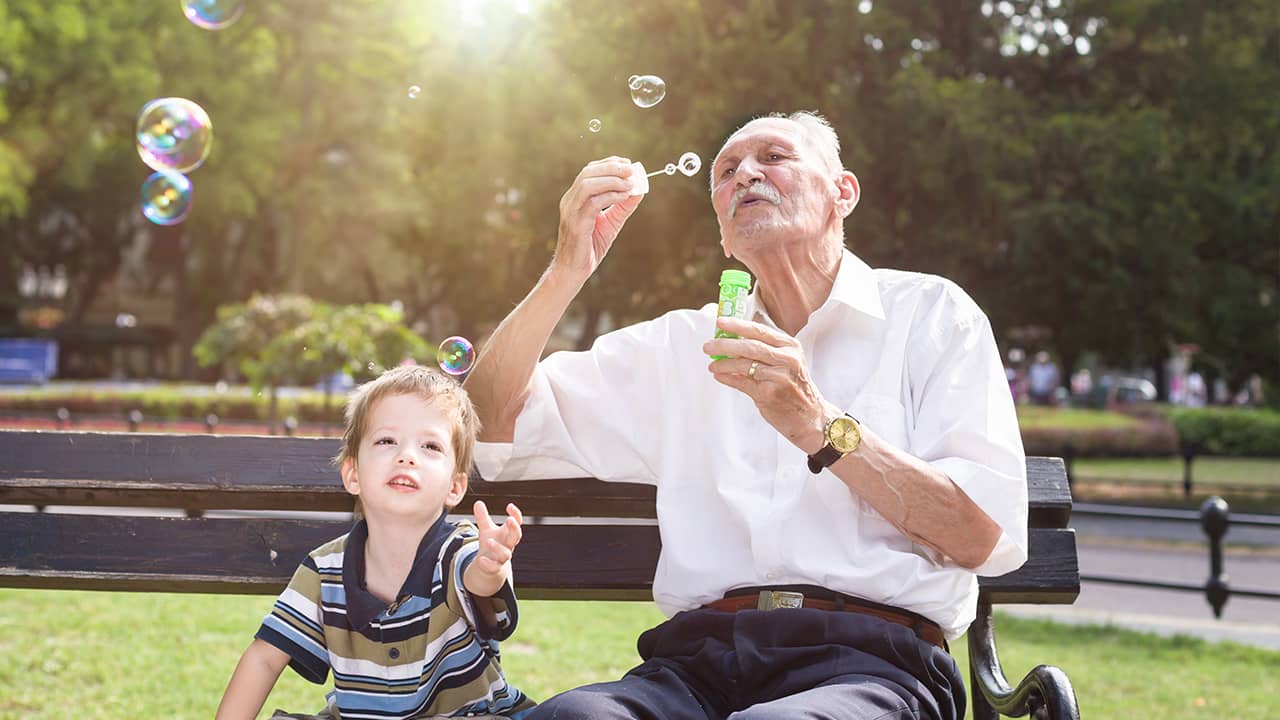 Photo of child with older man blowing bubbles in a park