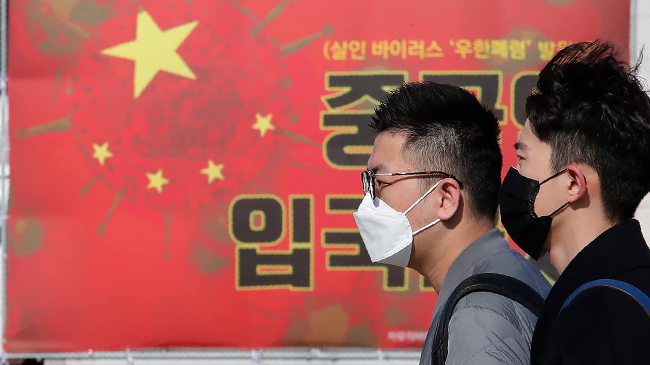 Photo of people passing by a China's flag with a virus image