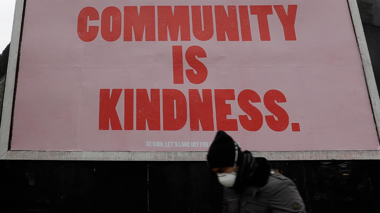 Photo of a man wearing a mask walking past a sign in London 