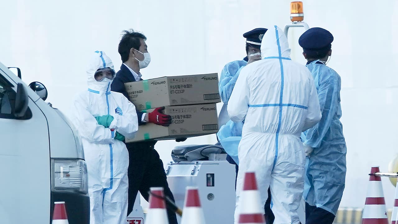 Photo of masked officials carrying boxes of digital thermometers 