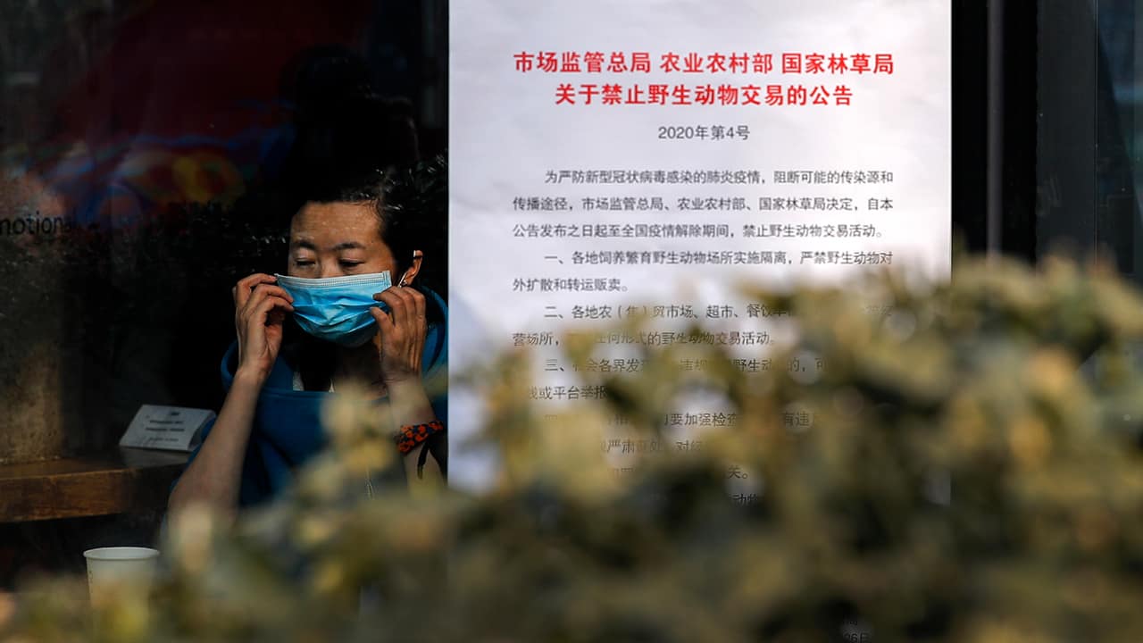 Photo of a woman putting on a mask near a notice board 