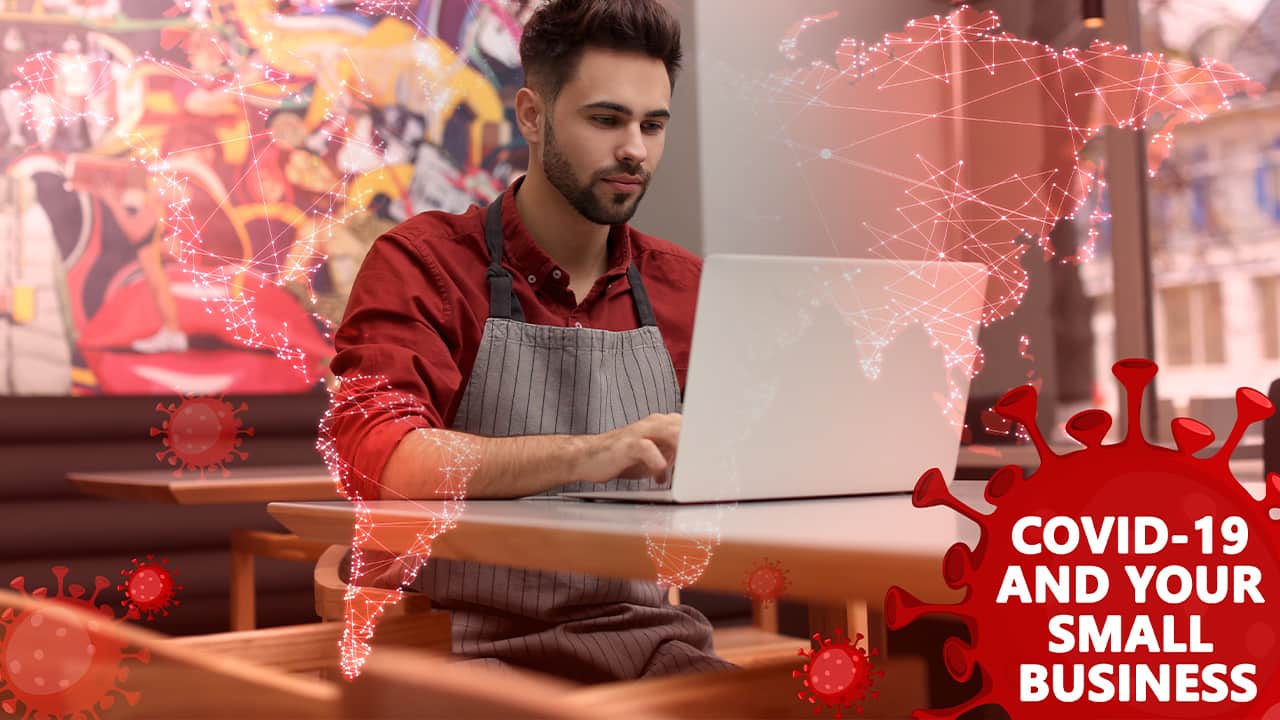 Composite image of a small businessman at laptop and COVID-19 symbols
