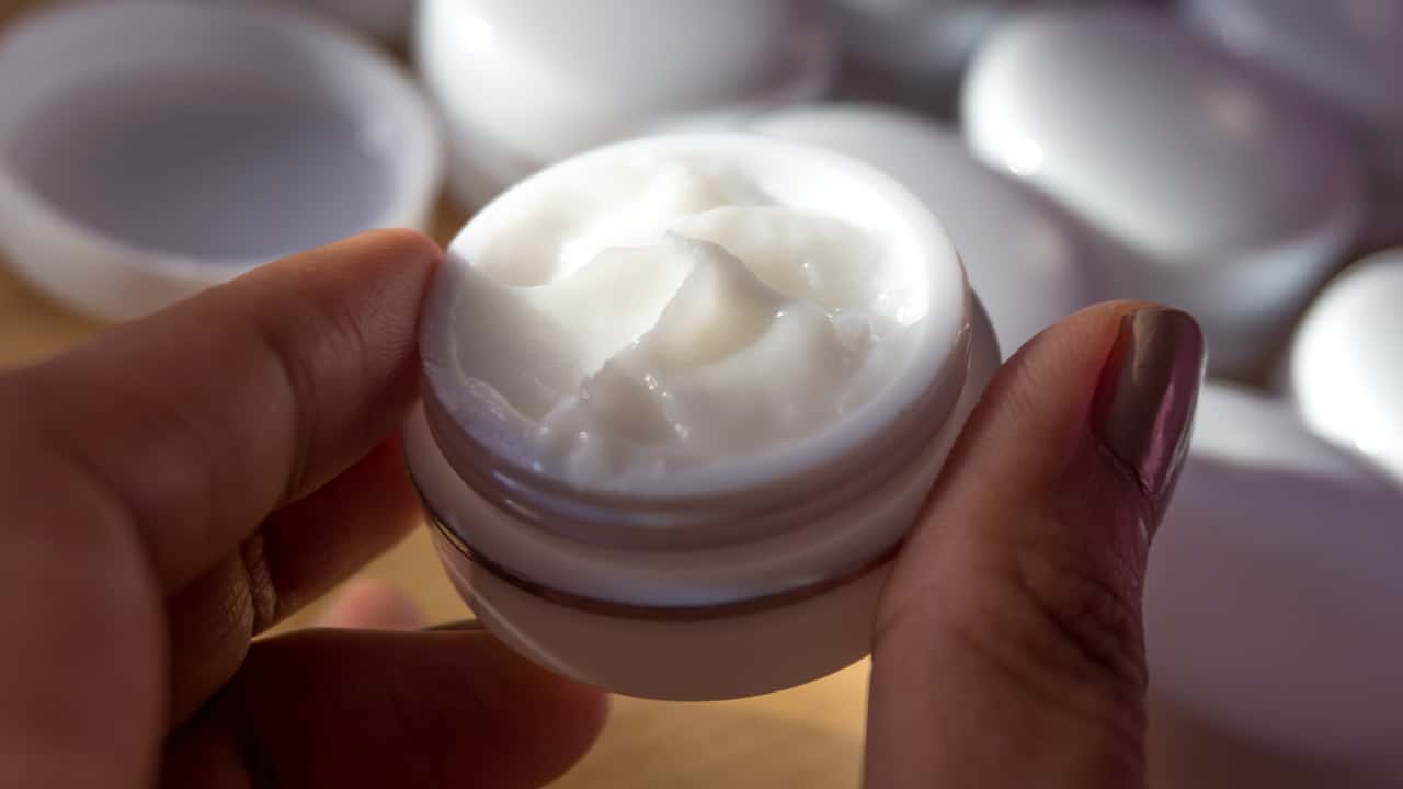 Photo of a small bottle of cream held between a thumb and a finger