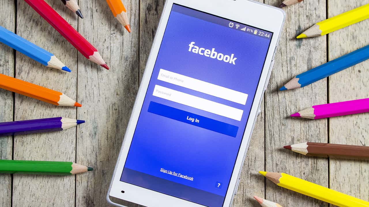 Photo of smartphone opened to Facebook sign-in page surrounded by colored pencils