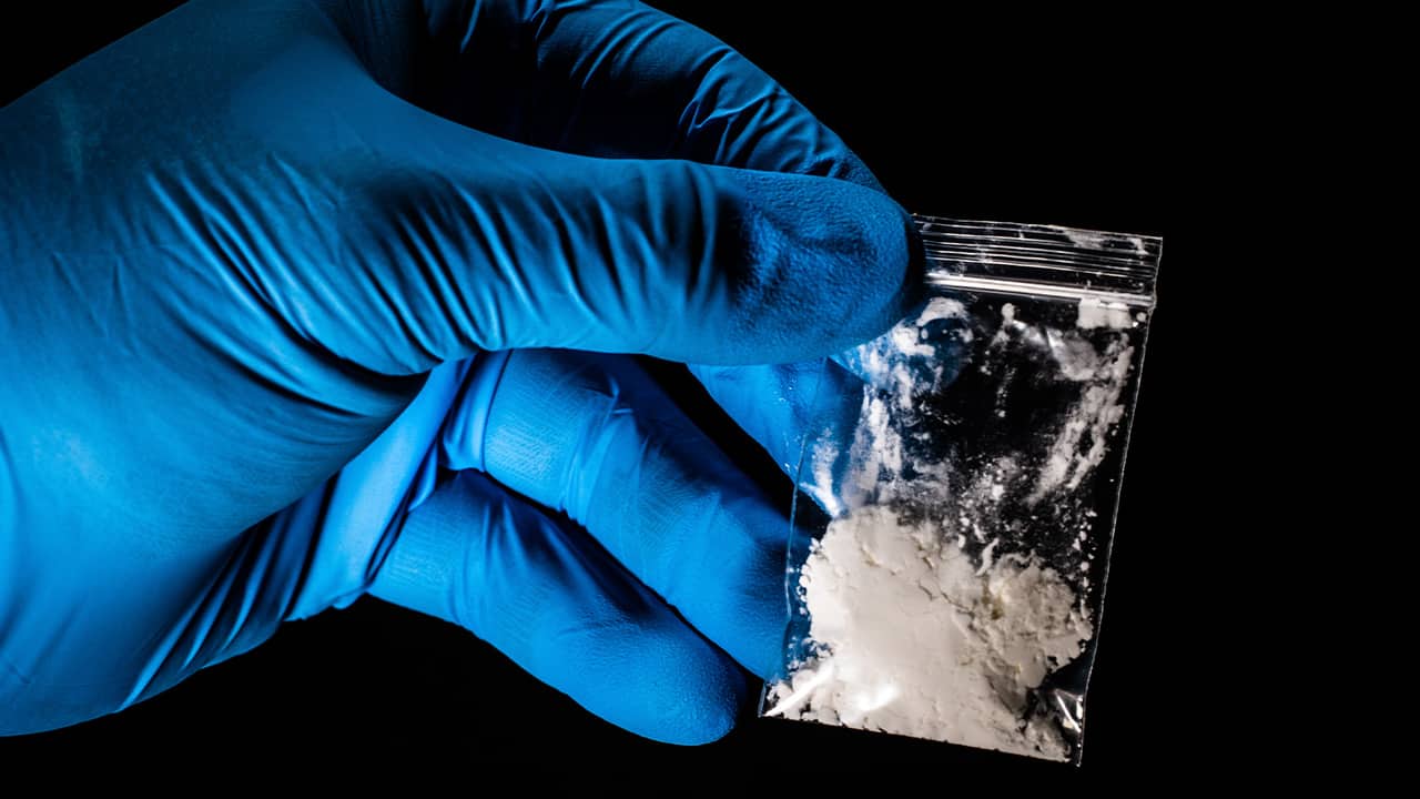 Photo of a gloved hand lifting up a package of powdered fentanyl