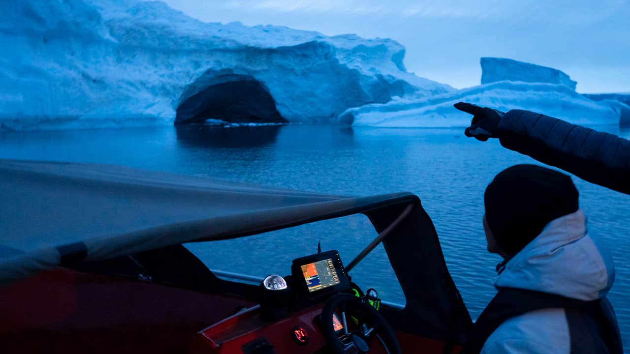 Photo of a boat navigating at night next to a large iceberg in Greenland