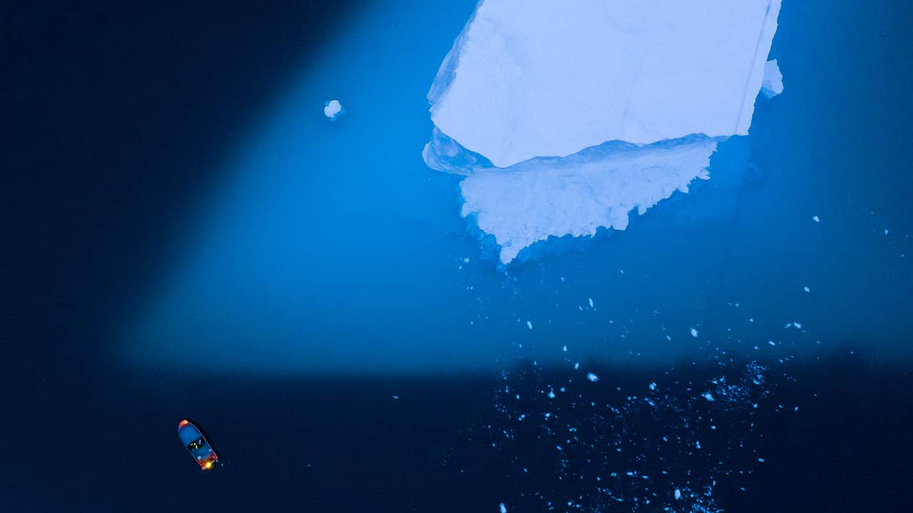 Photo of a boat navigating next to a large iceberg 