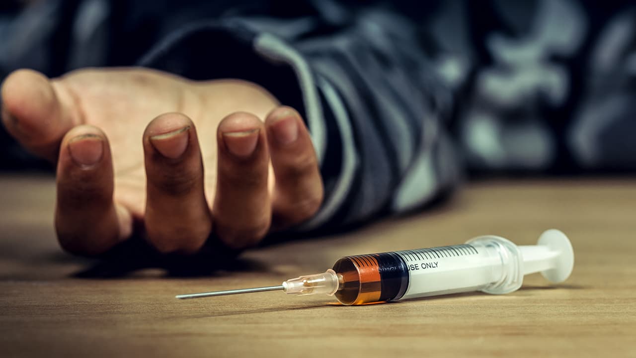 Photo of a man's hand and a heroin syringe