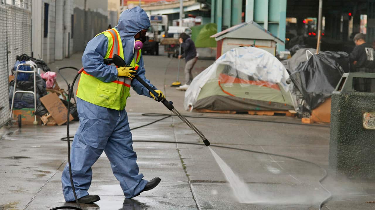 Photo of a city worker cleaning the sidewalk by a tent city