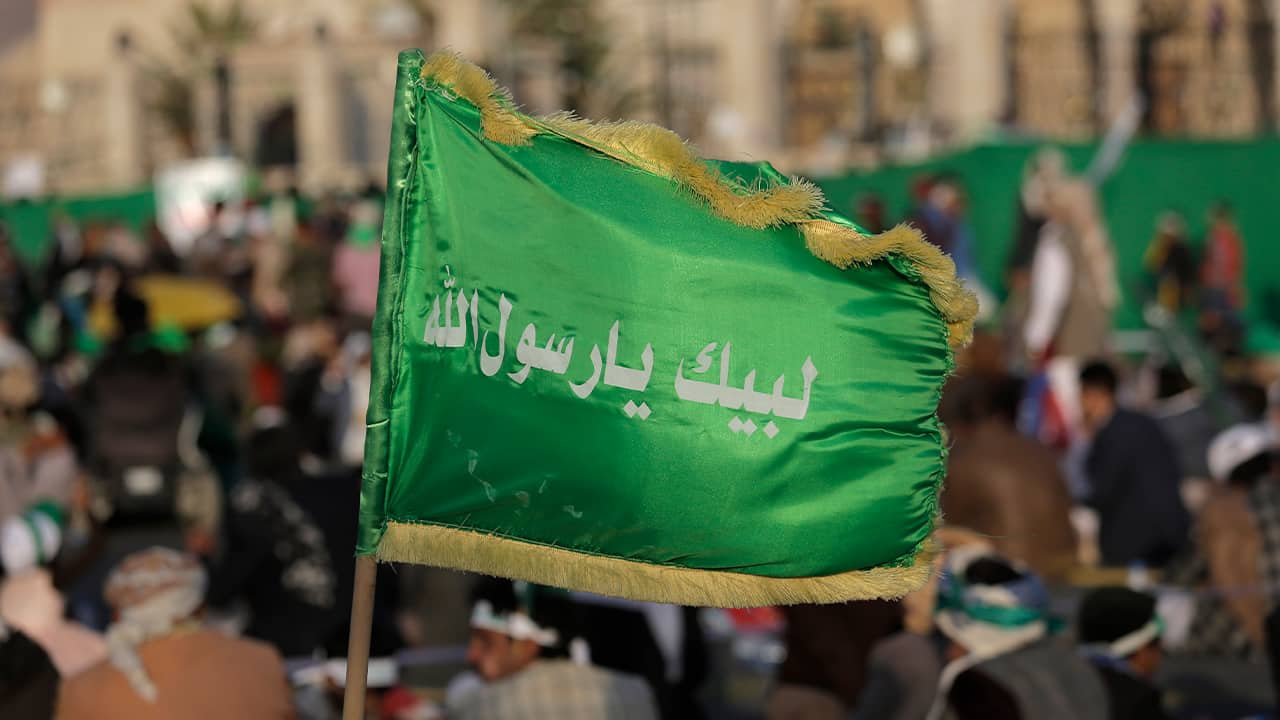 Photo of a Houthi supporter holding a banner with Arabic writing that reads, "at your order, oh messenger of Allah."