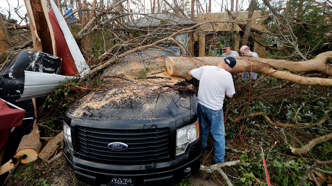 Photo of people cutting away at a tree the fell on a vehicle during Hurricane Michael