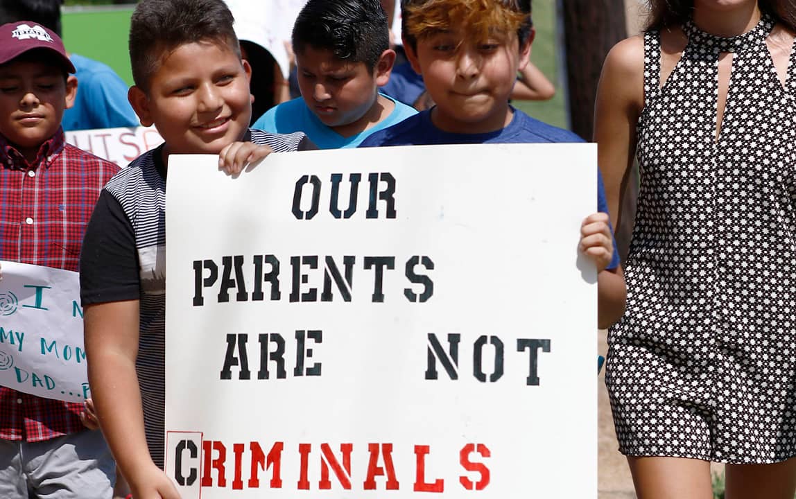 Photo of children holding signs in support of individuals picked up during immigration