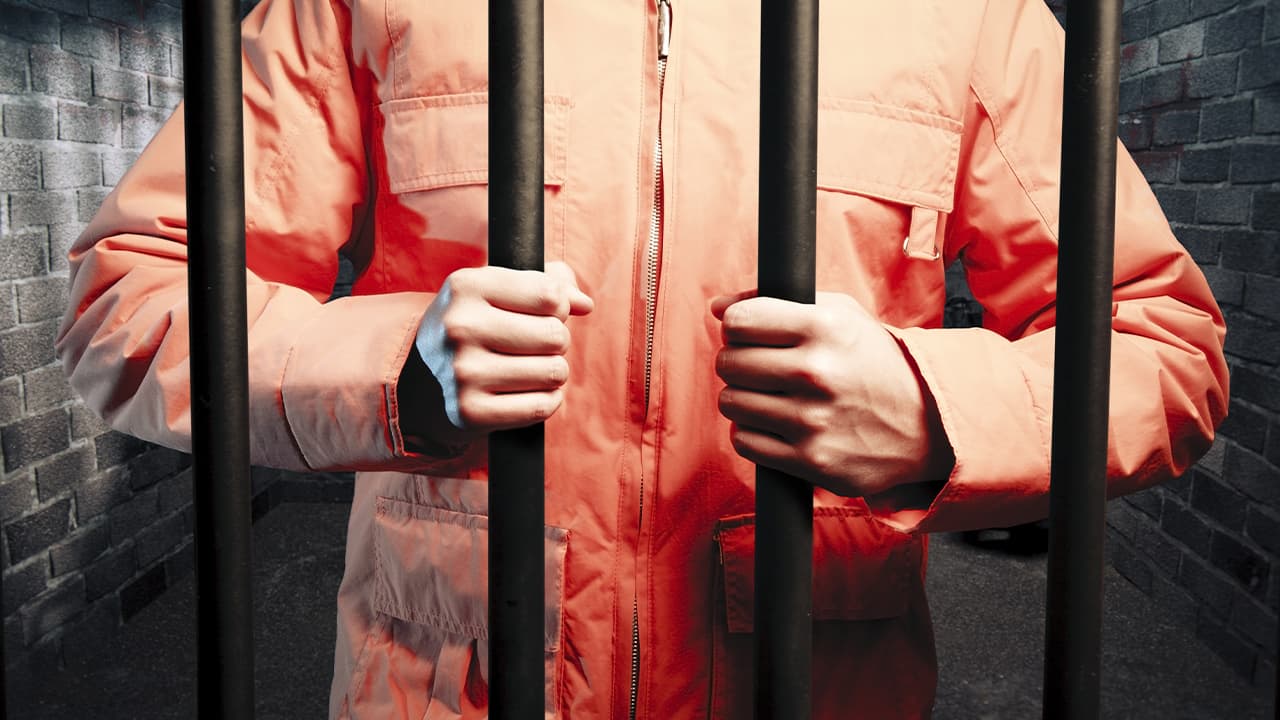 Photo of inmate in orange jumpsuit behind bars