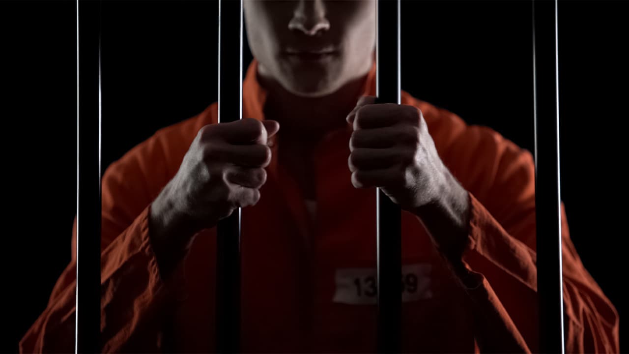 Photo of a man in an orange jumpsuit behind prison bars
