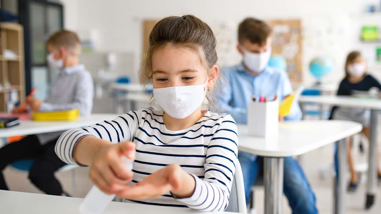 Image of a young student in a mask sanitizing her hands amid the coronavirus pandemic