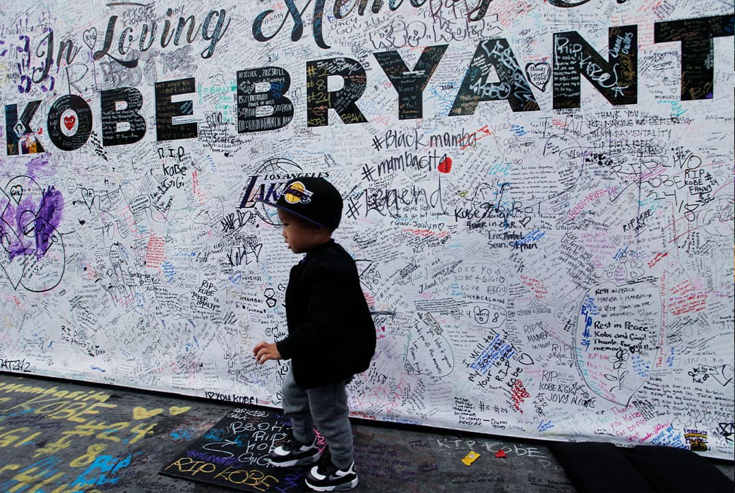 Photo of a boy walking by a standing board with messages for the late Kobe Bryant 