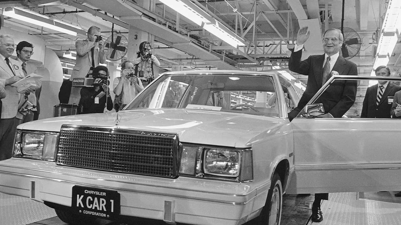 Photo of Lee Iacocca waving as he steps into the first K-Car in 1980 