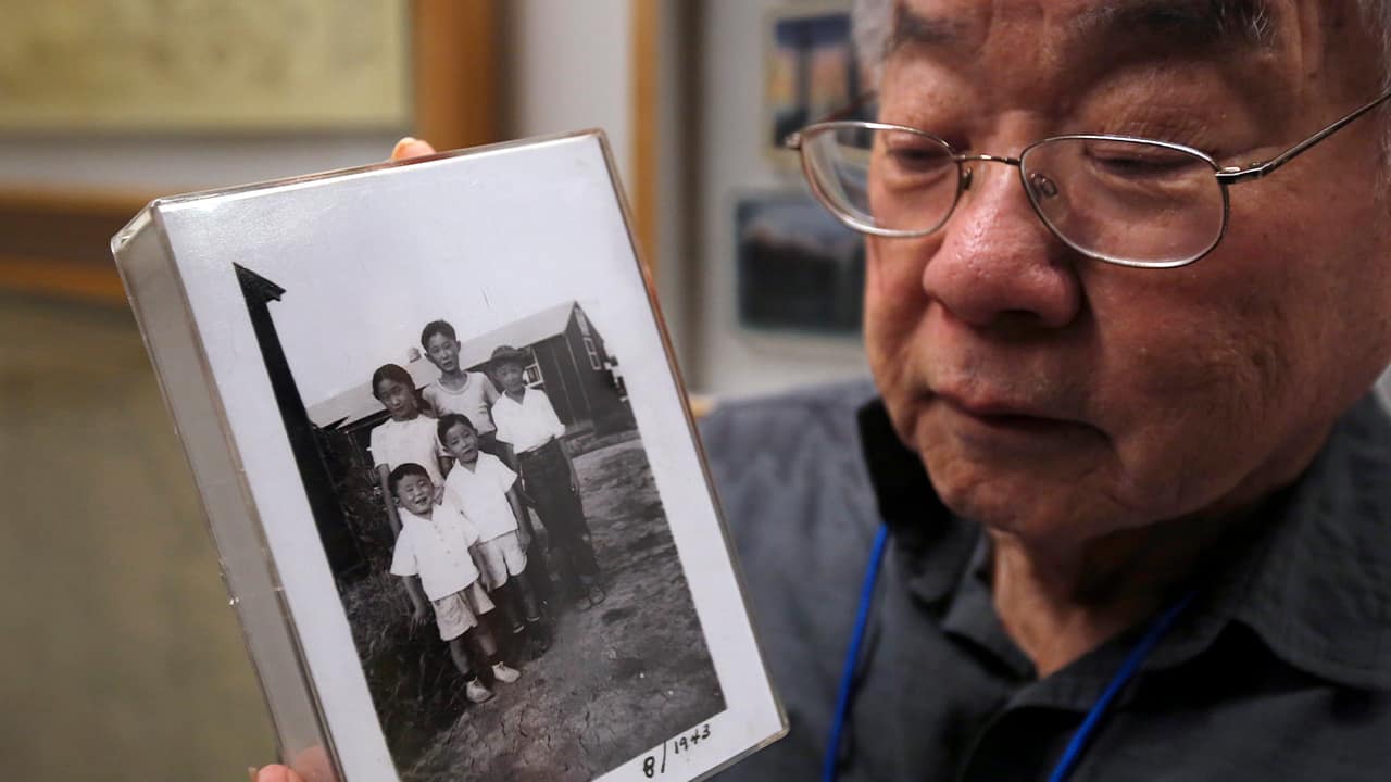 Photo of Les Ouchida holding a 1943 photo of himself, front row, center, and his siblings taken at the internment camp his family was moved to