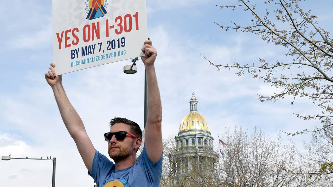 Photo of Chris Olson holding a sign in Denver