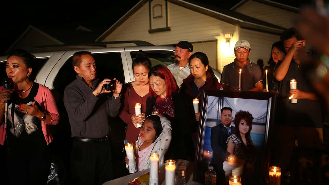 Photo of the wife and young daughter of shooting victim Kou Xiong standing among a crowd during a candle light vigil