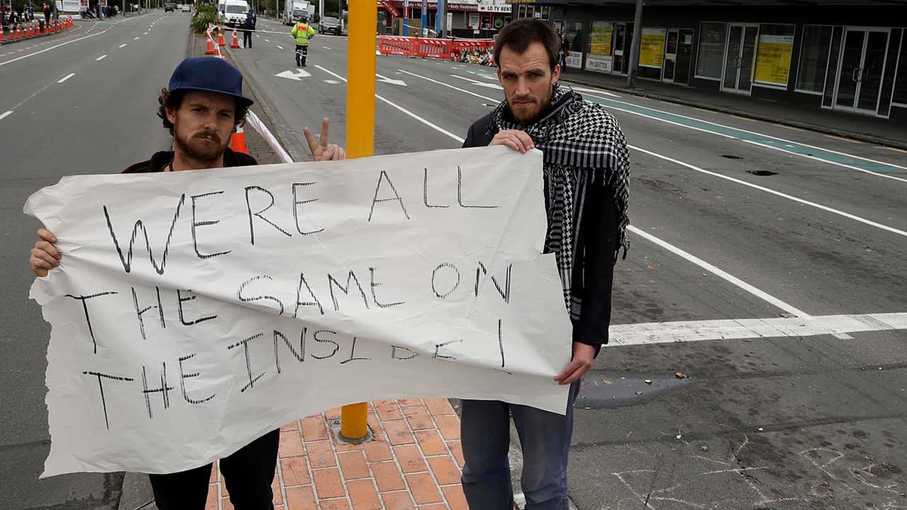 Photo of Linwood mosque shooting survivor Elliot Dawson, right, and a friend Shay Kenny holding a sign at an intersection