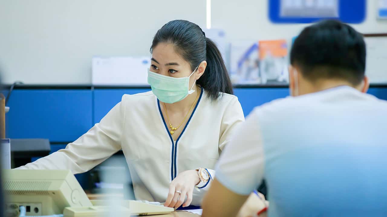 Image of a woman in a bank wearing a COVID-19 mask across from a customer