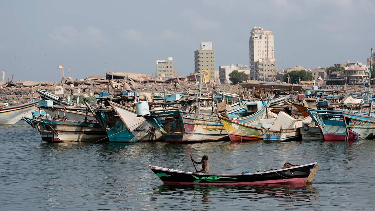 Photo of man paddling boat with Yemeni war wreckage in the background