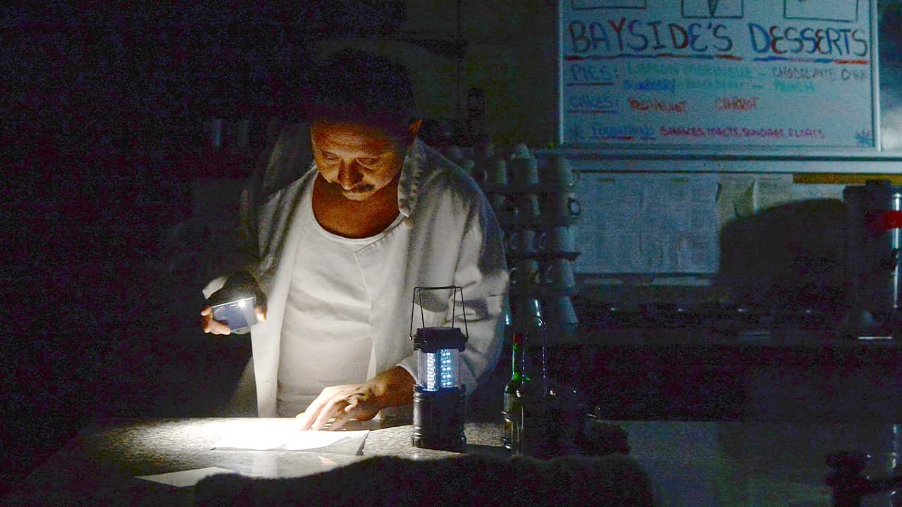 Photo of Carlos Lama using an LED lamp and his phone in his restaurant