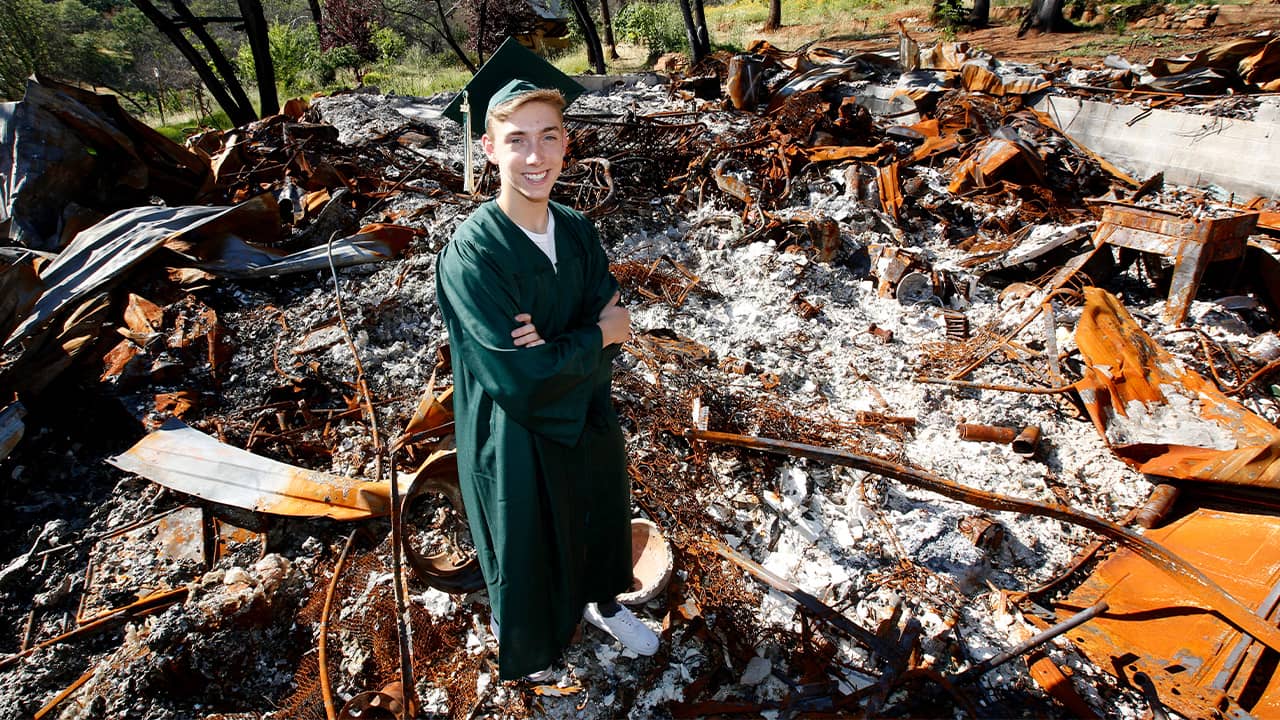 Photo of Sean Newsom posing at the burnout remains of his home in Paradise, CA